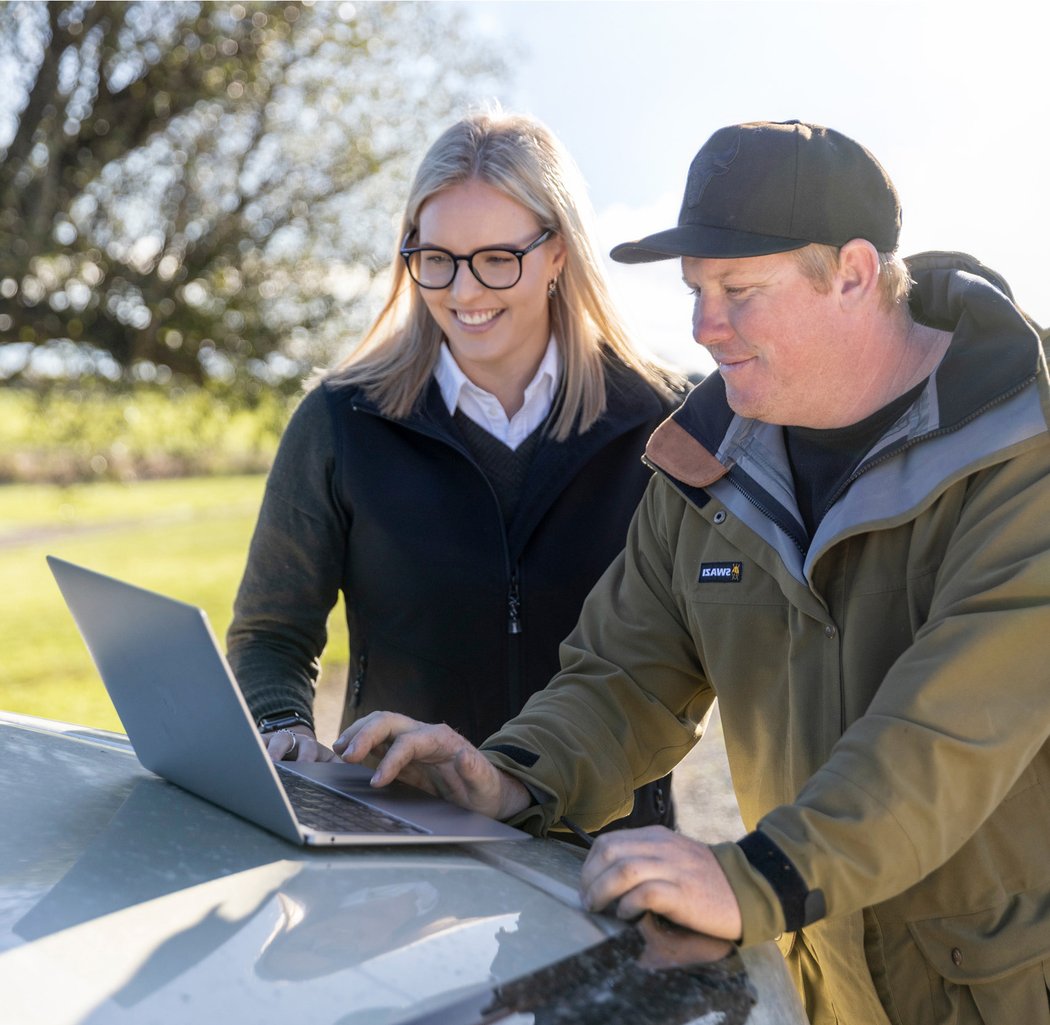 An adviser and a farmer going through farm figures on a laptop on the bonnet of a ute