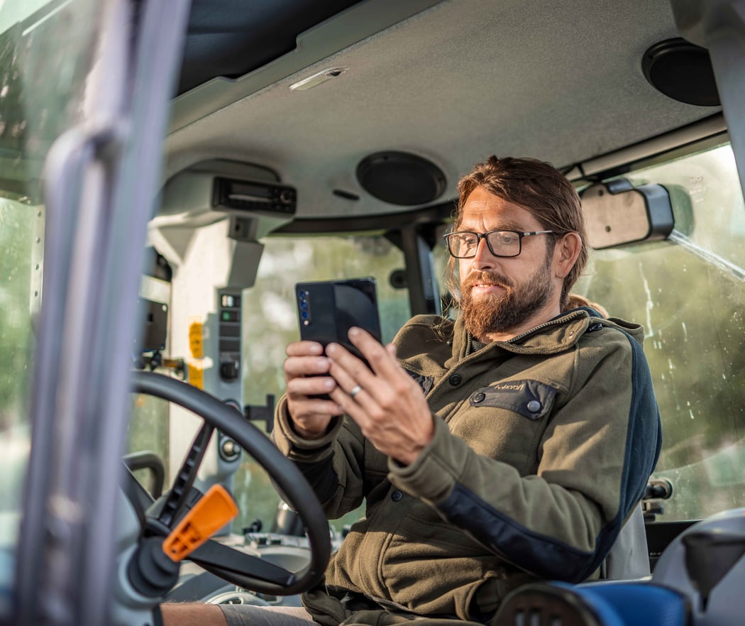 A farmer checking his farm figures on a phone from the cab of a tractor
